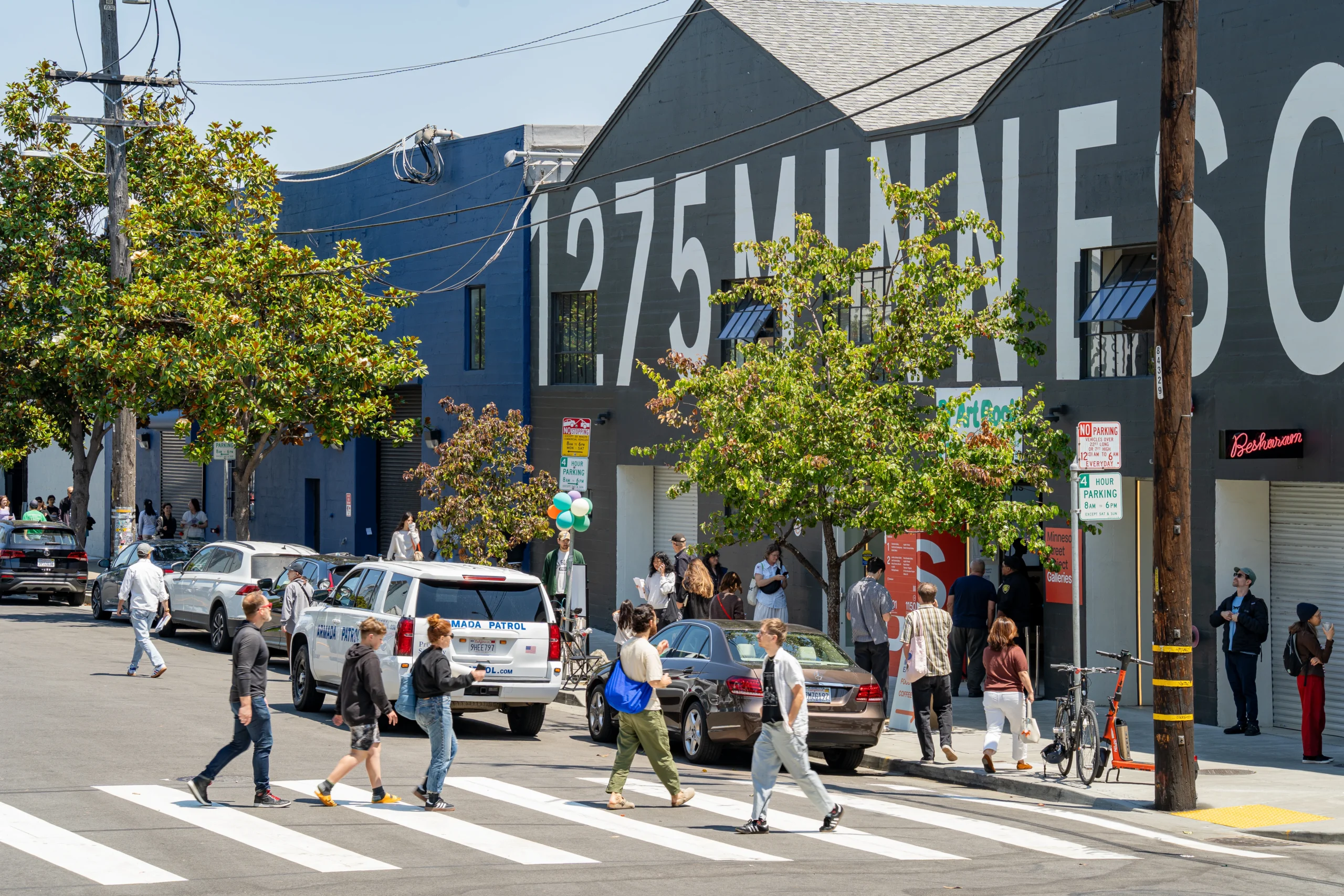 Visitors cross the street and gather outside 1275 Minnesota Street for the SF Art Book Fair, with an Armada Patrol vehicle parked curbside.