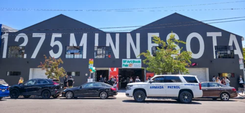 A white security SUV labeled “ARMADA PATROL” parked outside the SF Art Book Fair entrance at 1275 Minnesota Street, while attendees gather near the doors.