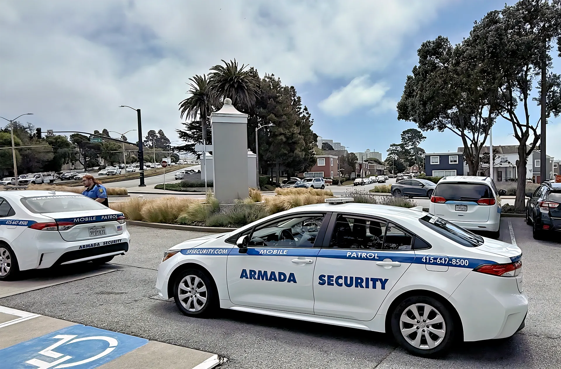 Armada Security mobile patrol vehicle parked, featuring clear branding and contact information, with a security officer nearby, set in a San Francisco urban environment.