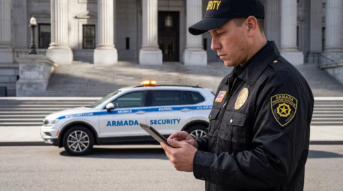Armada Security officer reviewing a tablet beside a marked patrol vehicle outside a San Francisco building with stone columns.